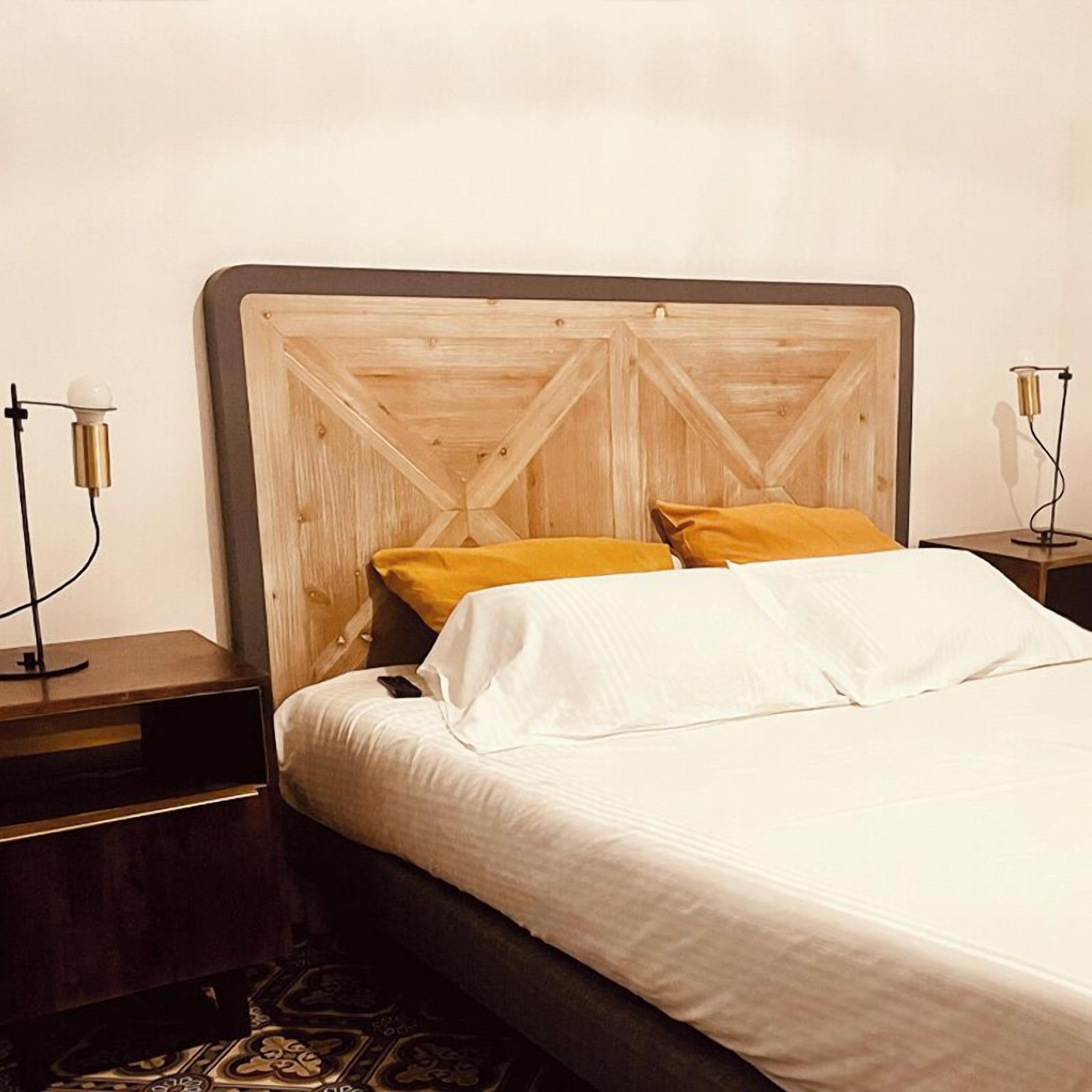A neatly made bed with white linens and two pillows, one yellow and one white, in a room with a wooden headboard and two bedside tables with lamps.