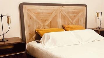 A neatly made bed with white linens and two pillows, one yellow and one white, in a room with a wooden headboard and two bedside tables with lamps.