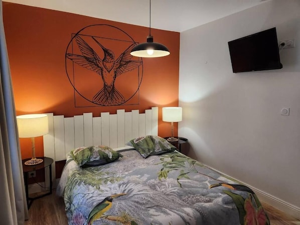 A bedroom with a bed, two bedside lamps, a wall-mounted TV, and a hanging pendant light.