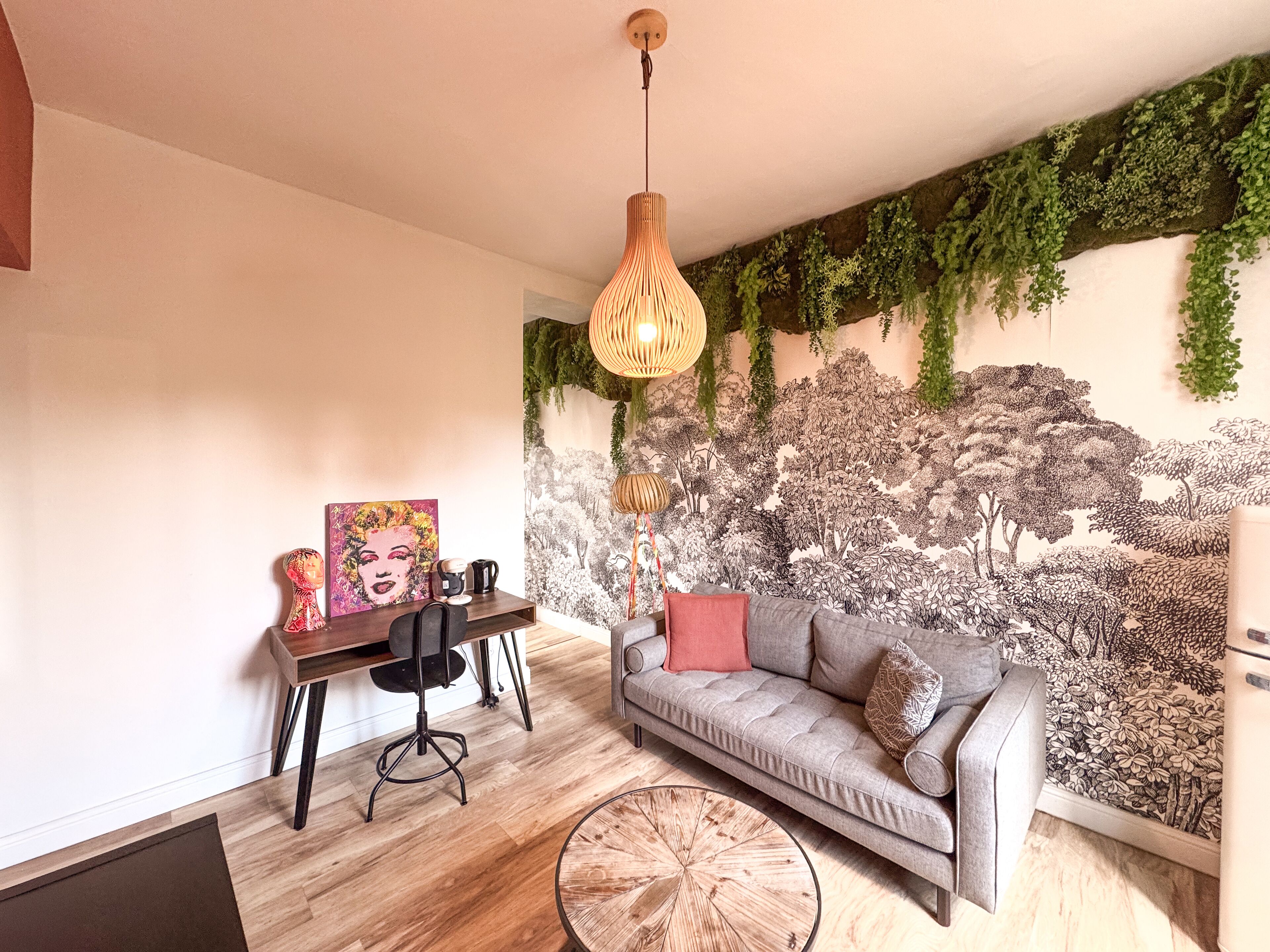 A modern living room with a grey sofa, a wooden coffee table, a desk with a chair, and a wall mural.