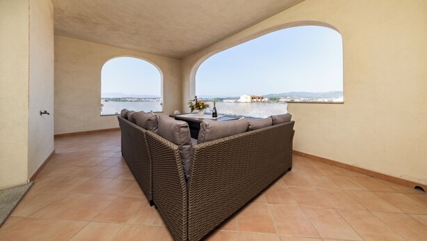 Un balcon avec un canapé en osier, une petite table sur laquelle est posé un vase, et une vue sur la ville et les collines.