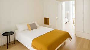 Una camera da letto minimalista con un letto, un comodino e una porta che conduce a un'altra stanza.