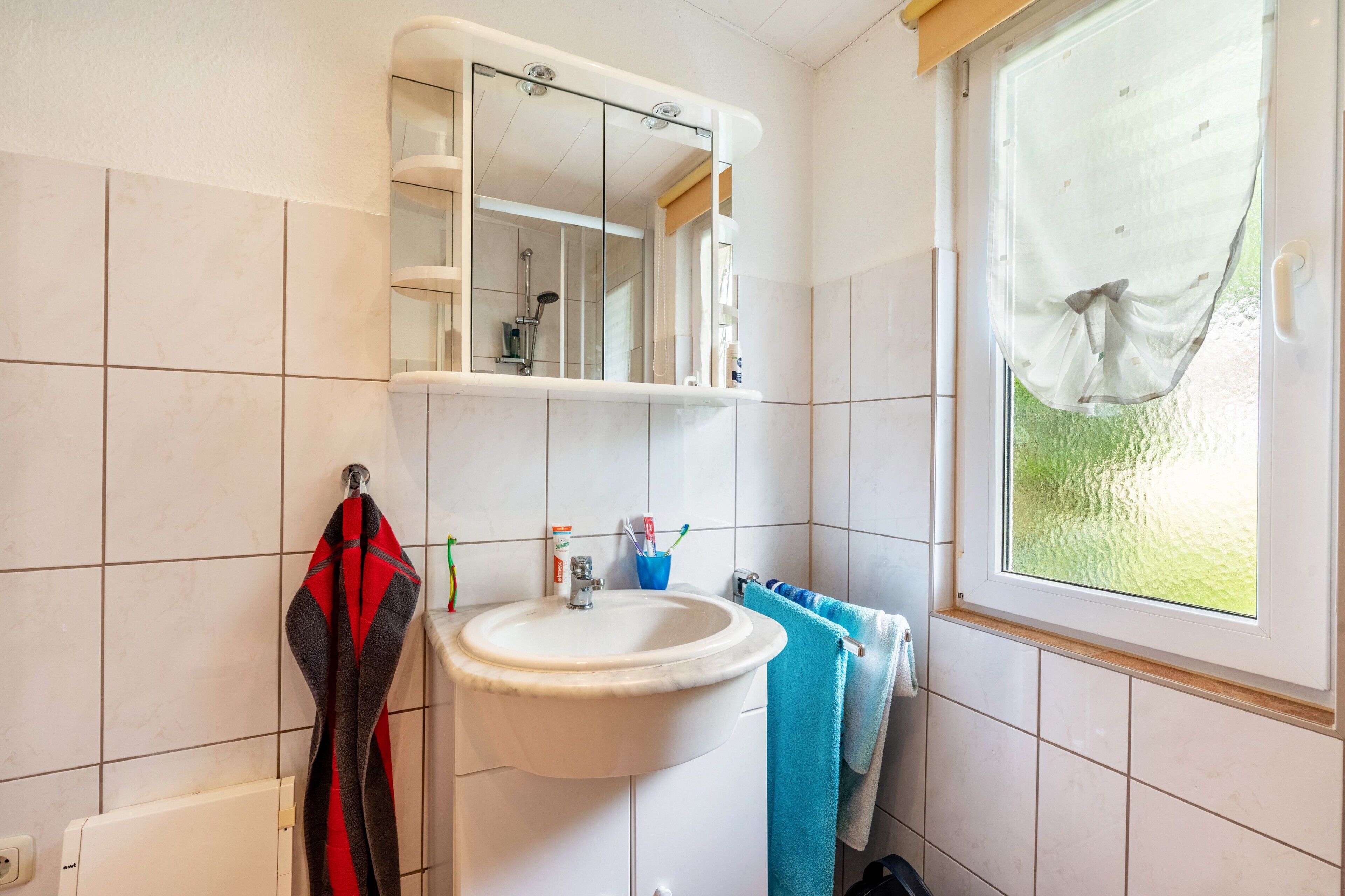 Une salle de bain avec un lavabo, un miroir et une fenêtre.