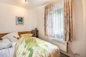 Un dormitorio con cama, mesita de noche, radiador y ventana con cortinas.