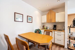 Cocina compacta con armarios de madera, una mesa de comedor con sillas y dos cuadros en la pared.
