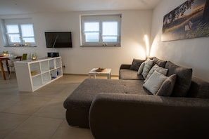 A living room with a sofa, a TV, a bookshelf, and a window with blinds.