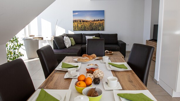 Un espace repas moderne avec une table en bois mise pour le petit-déjeuner, un canapé et un tableau accroché au mur.