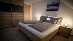 Un lit double avec un cadre en bois, deux tables de chevet, une commode et un tableau au mur.