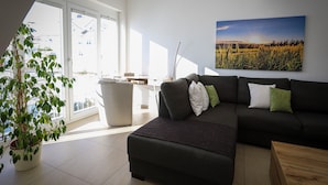 Un salon moderne avec un canapé d’angle, une plante en pot et une grande fenêtre.