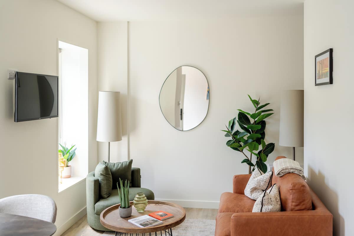 A modern living room with a sofa, armchair, coffee table, and a flat-screen TV mounted on the wall.
