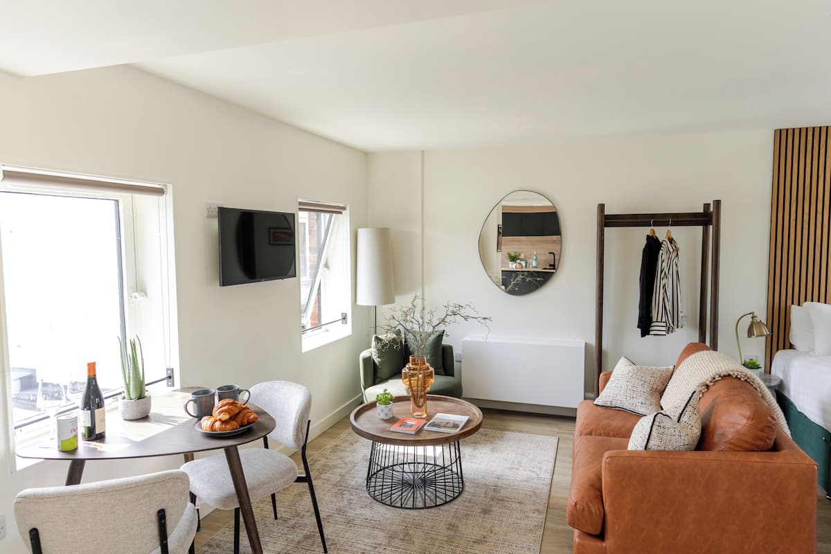 A modern living room with a sofa, a coffee table, a dining table with chairs, a TV, and a window with curtains.