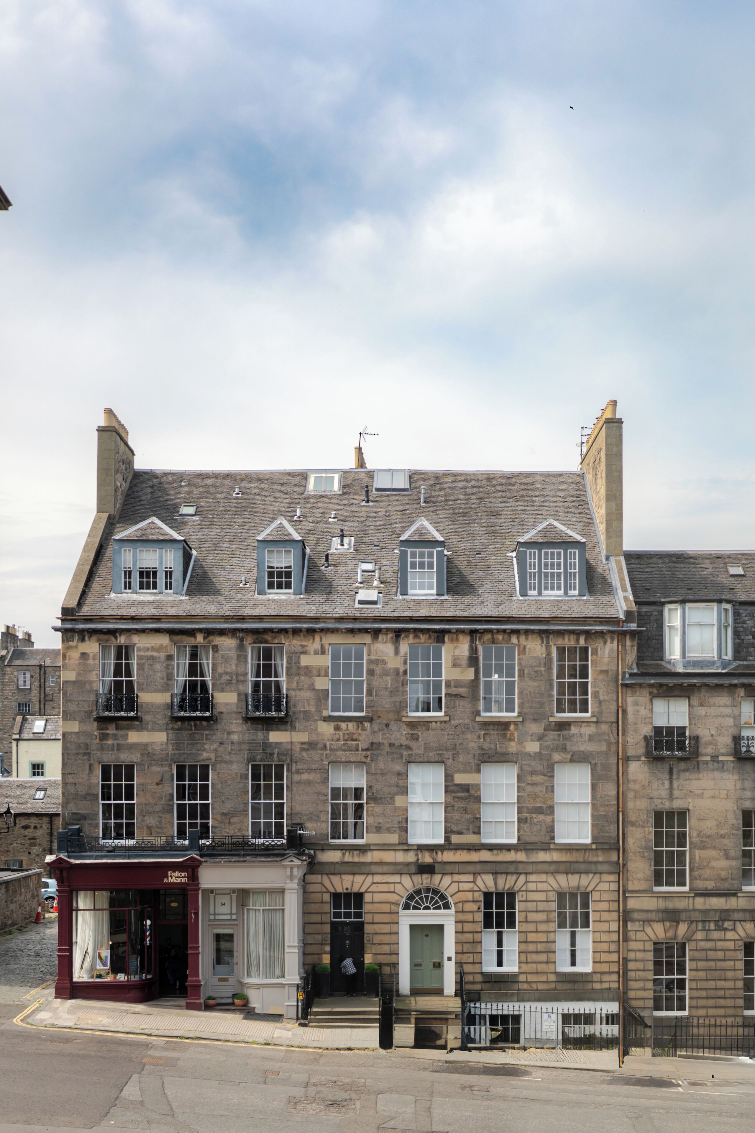 Un immeuble en pierre à plusieurs étages, de style architectural traditionnel, doté de nombreuses fenêtres et abritant un commerce au coin de la rue.