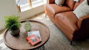Un salon chaleureux avec un canapé en cuir marron, une table basse ronde en bois, une plante en pot et un livre intitulé « Écosse ».