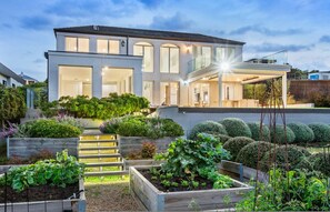 A modern two-story house with a large front porch, a covered outdoor seating area, and a well-maintained garden with raised beds and various plants. - Mount Martha Manor Indoor Pool Ocean Views (Melbourne)