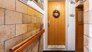 Een hal met een houten deur, een houten leuning, een betegelde muur en een rieten mand aan de muur.