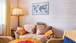 Een kamer met een bank, een lamp, een rieten stoel en een wereldkaart aan de muur.