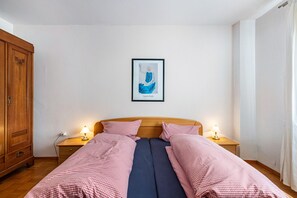 Une chambre avec une armoire en bois, un lit avec une literie à carreaux, deux lampes de chevet et une œuvre d’art encadrée au mur.