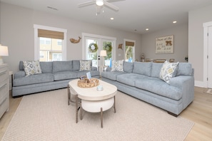 A modern living room with a grey sectional sofa, a round coffee table, and a white rug. - New Construction, 5 Bedroom, Private Pool - Down At The Lah De Dah (Surfside Beach)