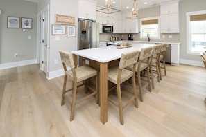 A modern kitchen with white cabinets, stainless steel appliances, and a central island with bar stools. - New Construction, 5 Bedroom, Private Pool - Down At The Lah De Dah (Surfside Beach)