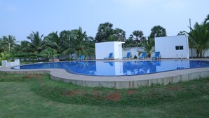Una piscina con agua azul, rodeada de césped y palmeras.