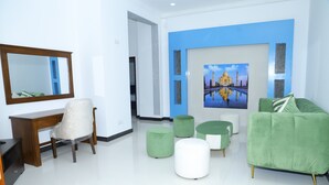 Un salón moderno con un sofá verde, un escritorio de madera, una silla blanca y un cuadro grande de un edificio en la pared.