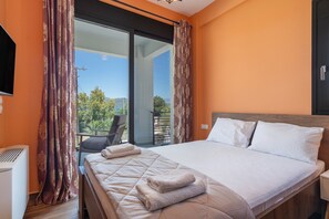 A hotel room with a large bed, a TV, and a balcony with a view of greenery.