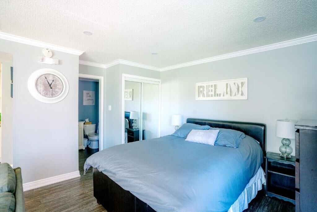 A bedroom with a bed, a clock, a mirror, and a wall sign.