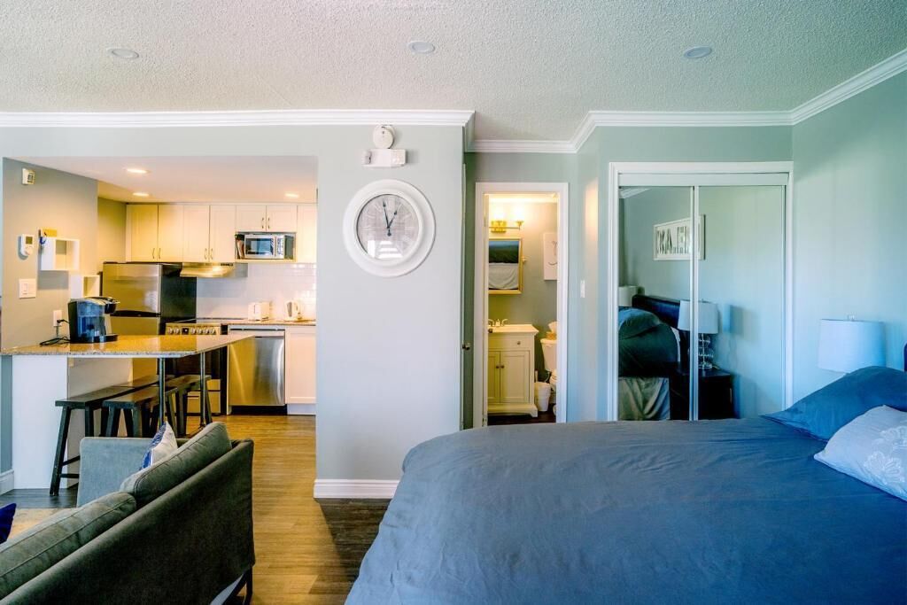 A compact hotel room with a bed, a small kitchenette, and a bathroom visible through an open door.