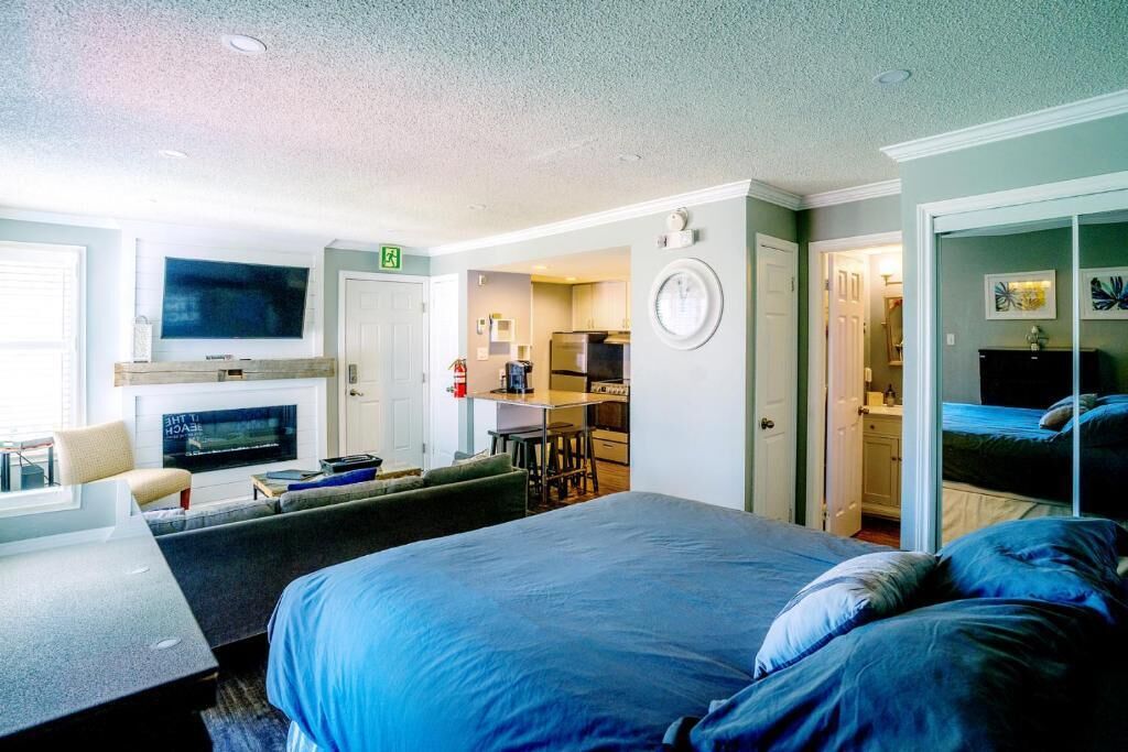 A hotel room with a bed, a sofa, a TV, a fireplace, a kitchen area, and a bathroom.