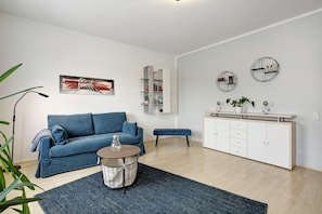 A modern living room with a blue sofa, a drum stool, a bookshelf, and a white cabinet.