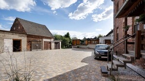 A courtyard with a paved area, a car, and buildings with brick facades and wooden doors. - Holiday Apartment 'Spree - Oase' in Spremberg (Spremberg)