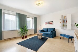 A modern living room with a blue sofa, a round coffee table, a blue rug, and a bookshelf.