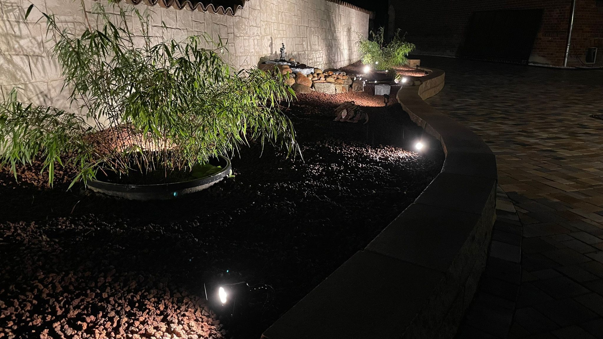 Een tuin 's nachts met waterpartijen, beplanting en een stenen muur.