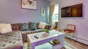 A living room with a tufted sofa, a coffee table with a plant, and a television mounted on the wall. - 3 Mi to Dtwn Newark: Eclectic & Walkable Apt! (Newark)