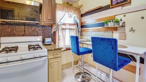 A kitchen with a stove, cabinets, and a window with curtains. There are two blue chairs and a small table. - 3 Mi to Dtwn Newark: Eclectic & Walkable Apt! (Newark)