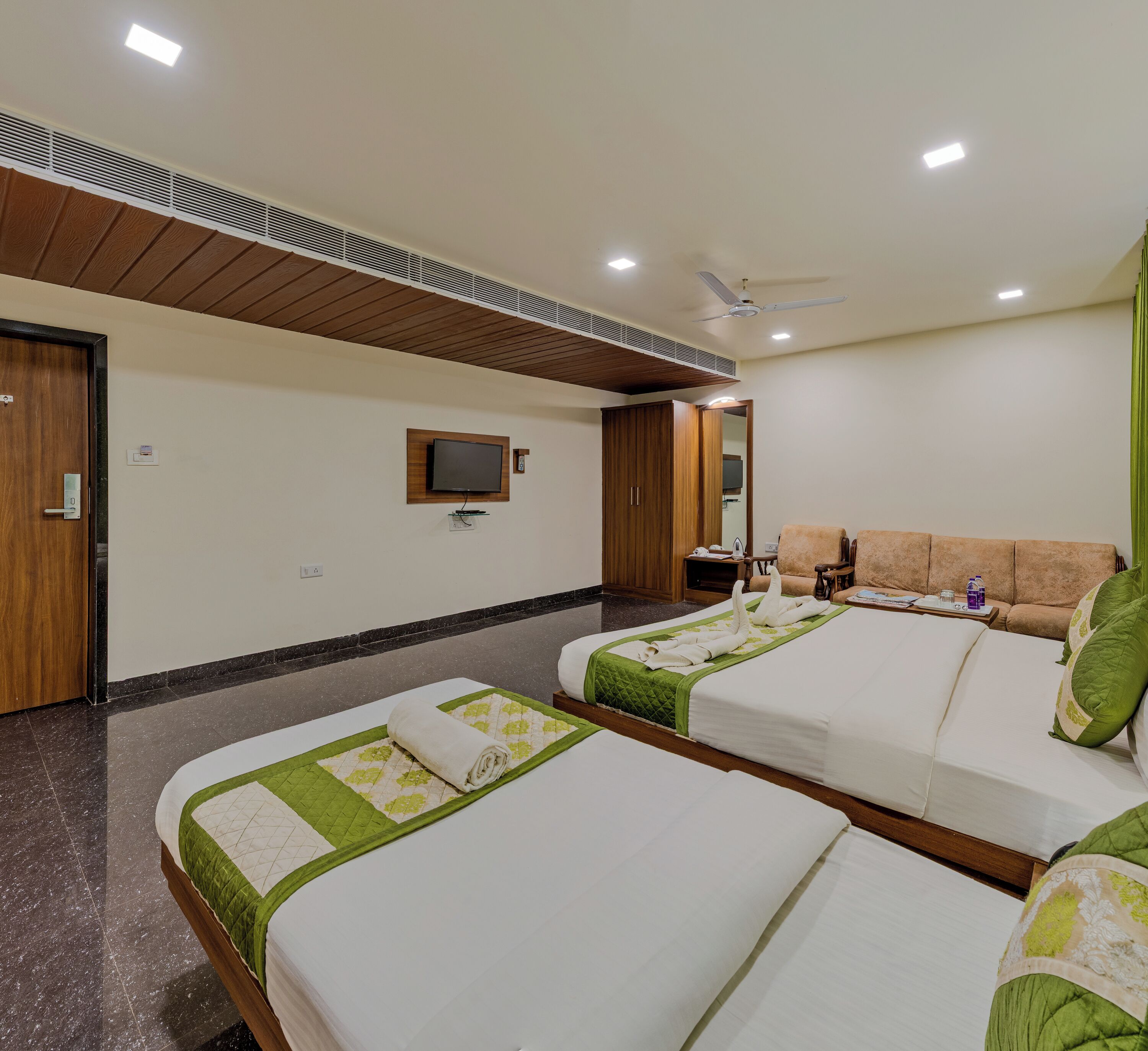 A hotel room with two beds, a TV mounted on the wall, a ceiling fan, and a wardrobe.