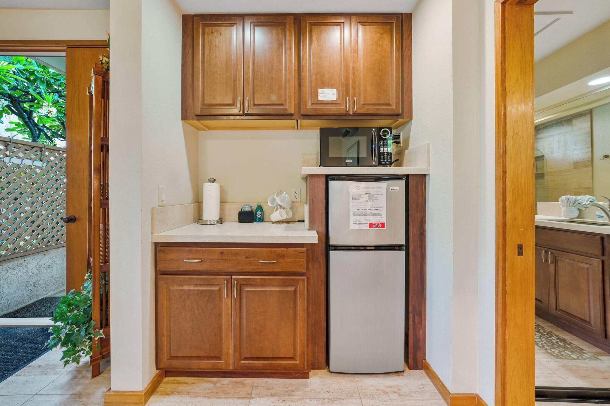 A compact kitchen with wooden cabinets, a stainless steel refrigerator, and a microwave.