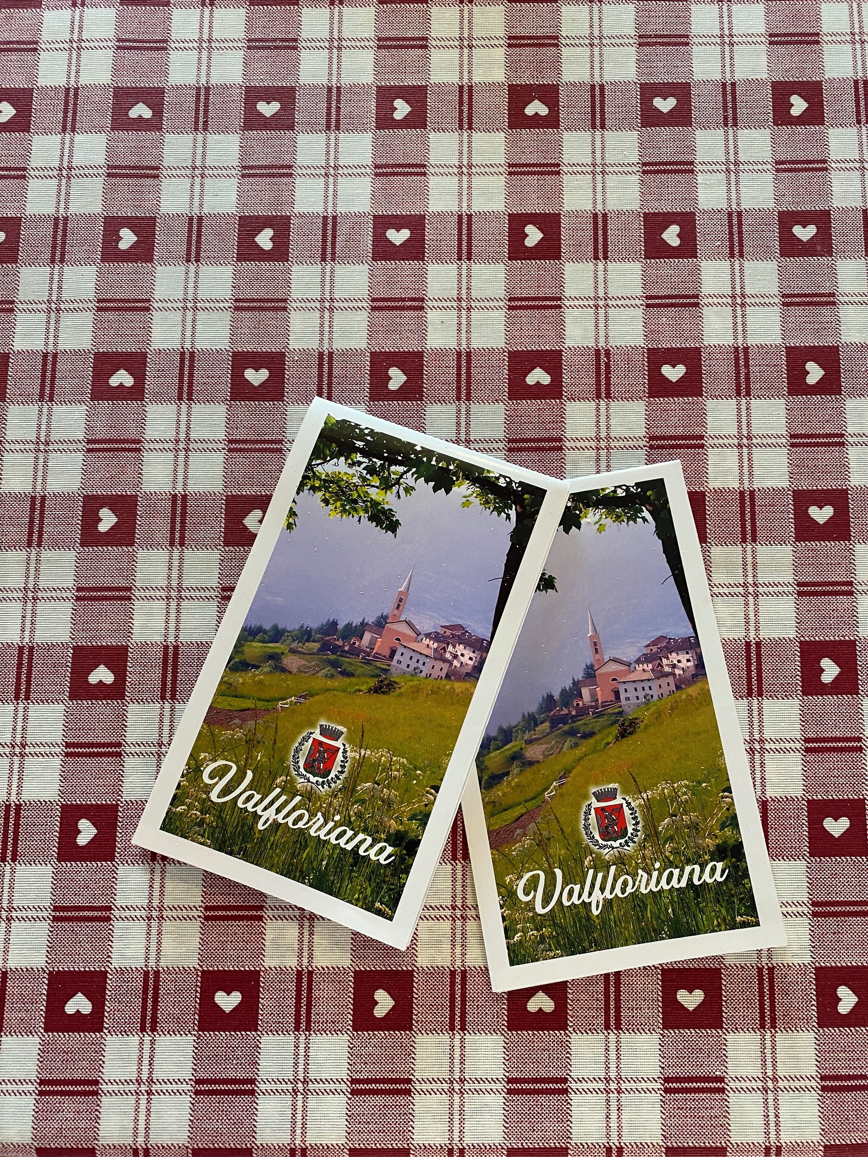 Zwei Postkarten mit Landschaft und Kirche vor einem karierten Stoffhintergrund.