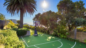 An outdoor basketball court surrounded by lush greenery and a palm tree. - Villa Luminosa in Mount Martha (Melbourne)