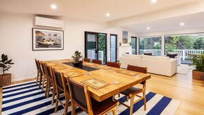 Een ruime eethoek met een houten tafel en stoelen, een blauw-wit gestreept vloerkleed en een groot raam met uitzicht op groen.