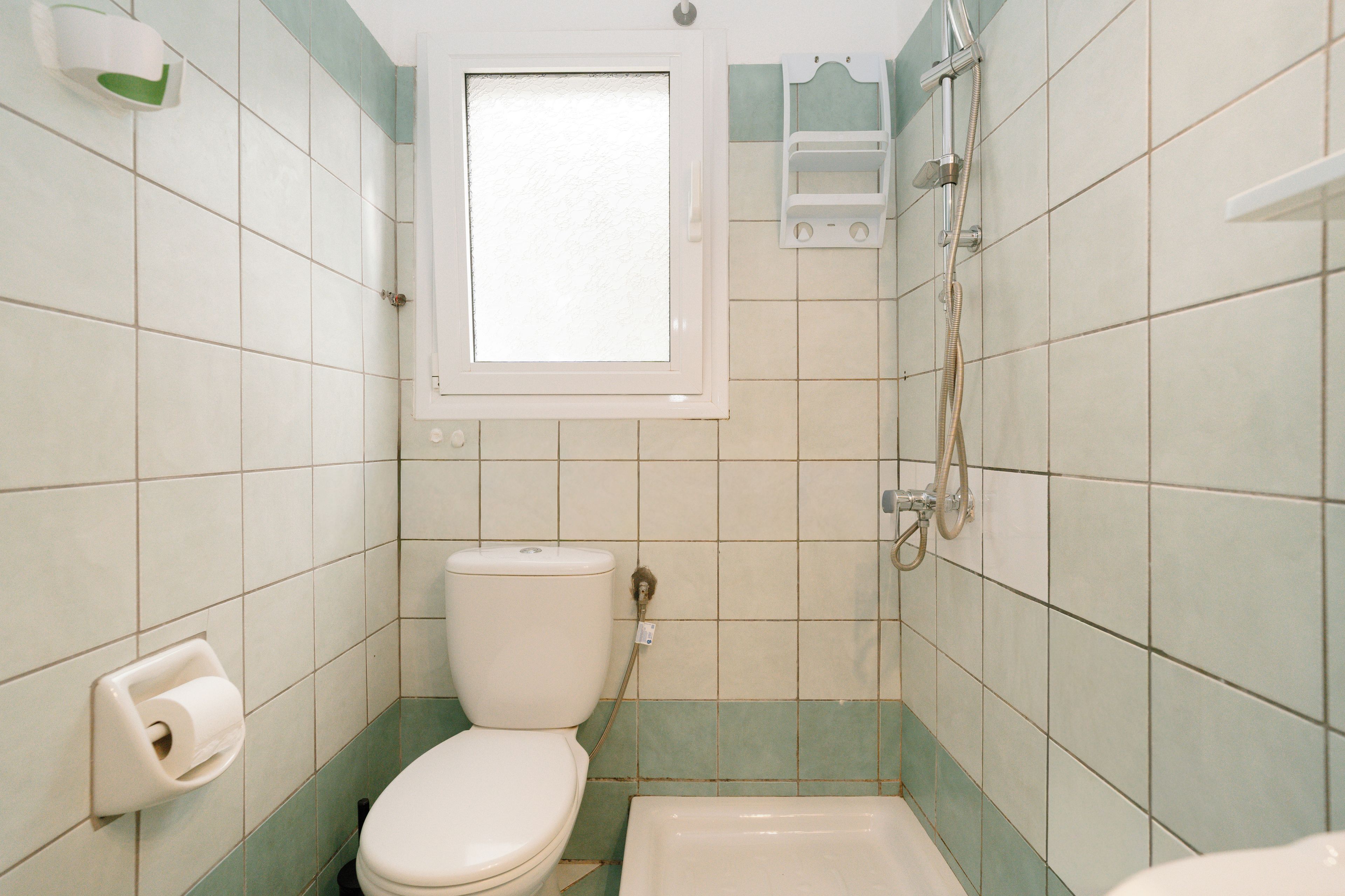 A small bathroom with a toilet, a shower, and a window.