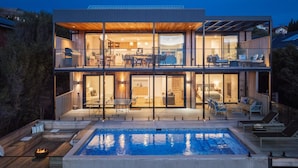 A modern two-story house with a large glass facade, a swimming pool, and outdoor seating areas. - Azure Horizon Gas Heated Pool With Stunning View (Melbourne)