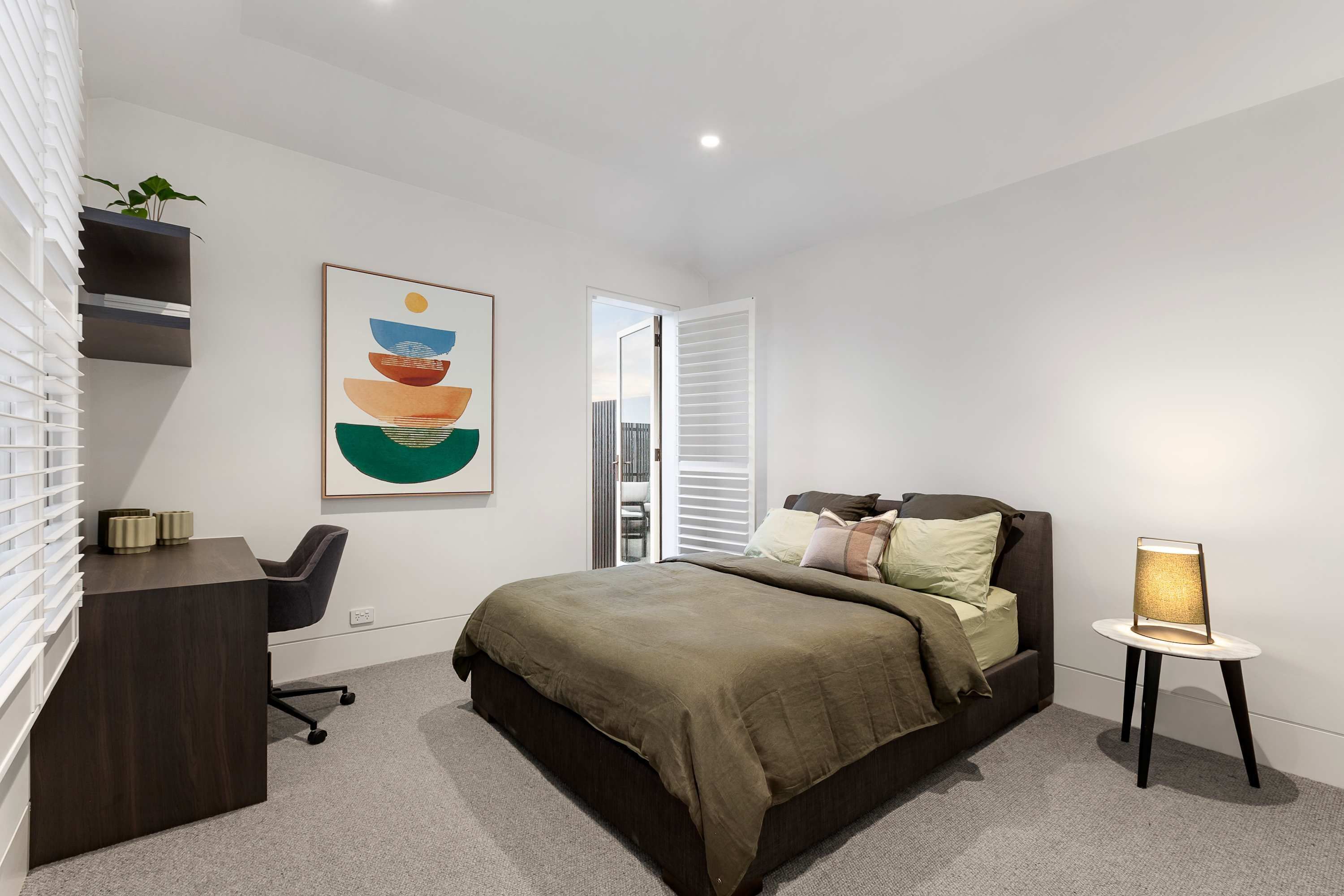 A modern bedroom with a bed, bedside table, chair, and a desk.