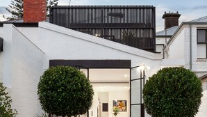 Une maison moderne avec une entrée dotée d’une porte en verre, un escalier menant à une terrasse et une pelouse bien entretenue.