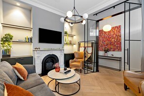 Een moderne woonkamer met een open haard, een bank, een salontafel en een aan de muur bevestigde televisie.