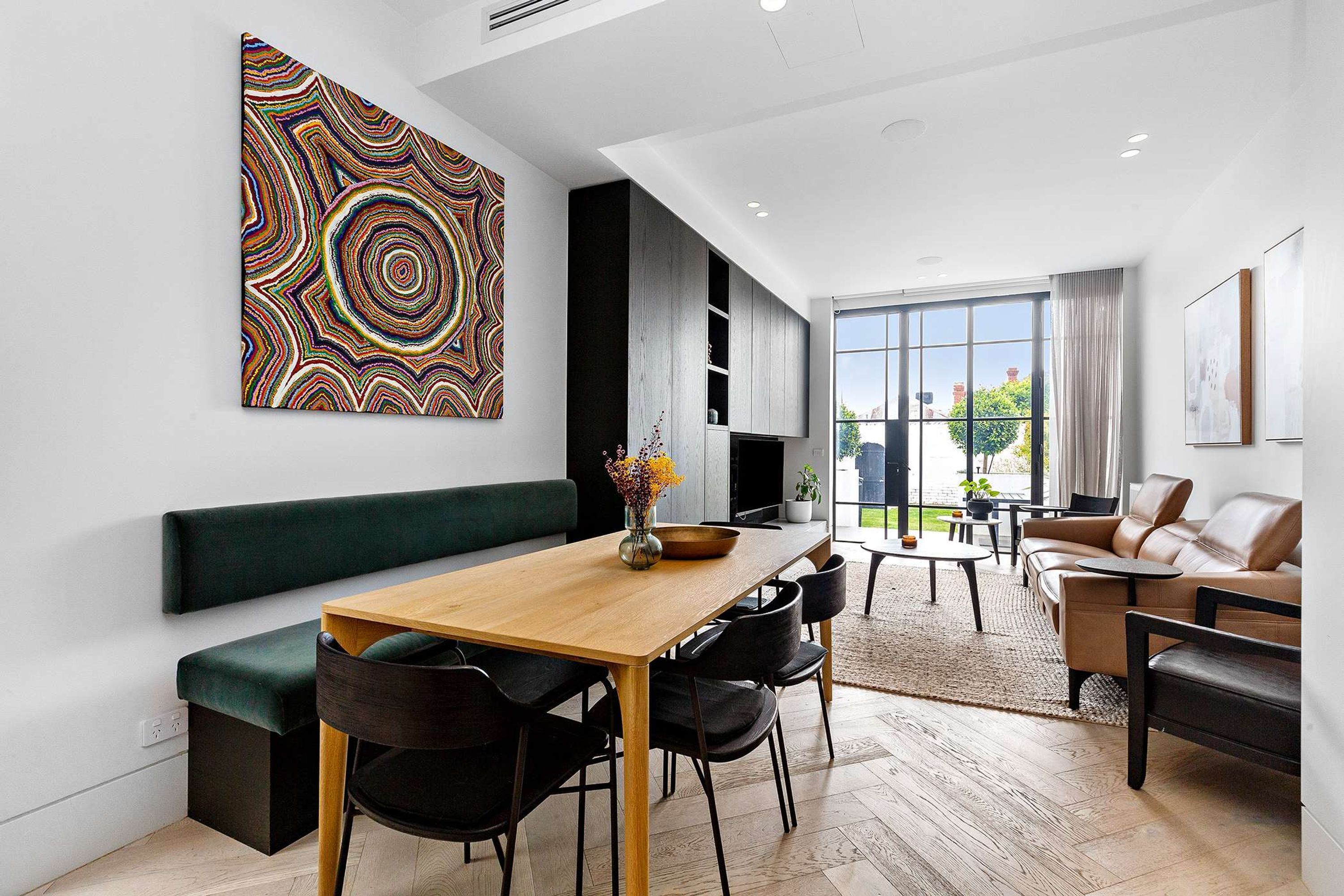 Un salón moderno con una mesa de comedor de madera, sillas negras, un banco verde y un cuadro abstracto grande en la pared.