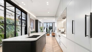 Une cuisine moderne dotée d’un grand îlot central, de meubles blancs et offrant une vue sur la verdure environnante.