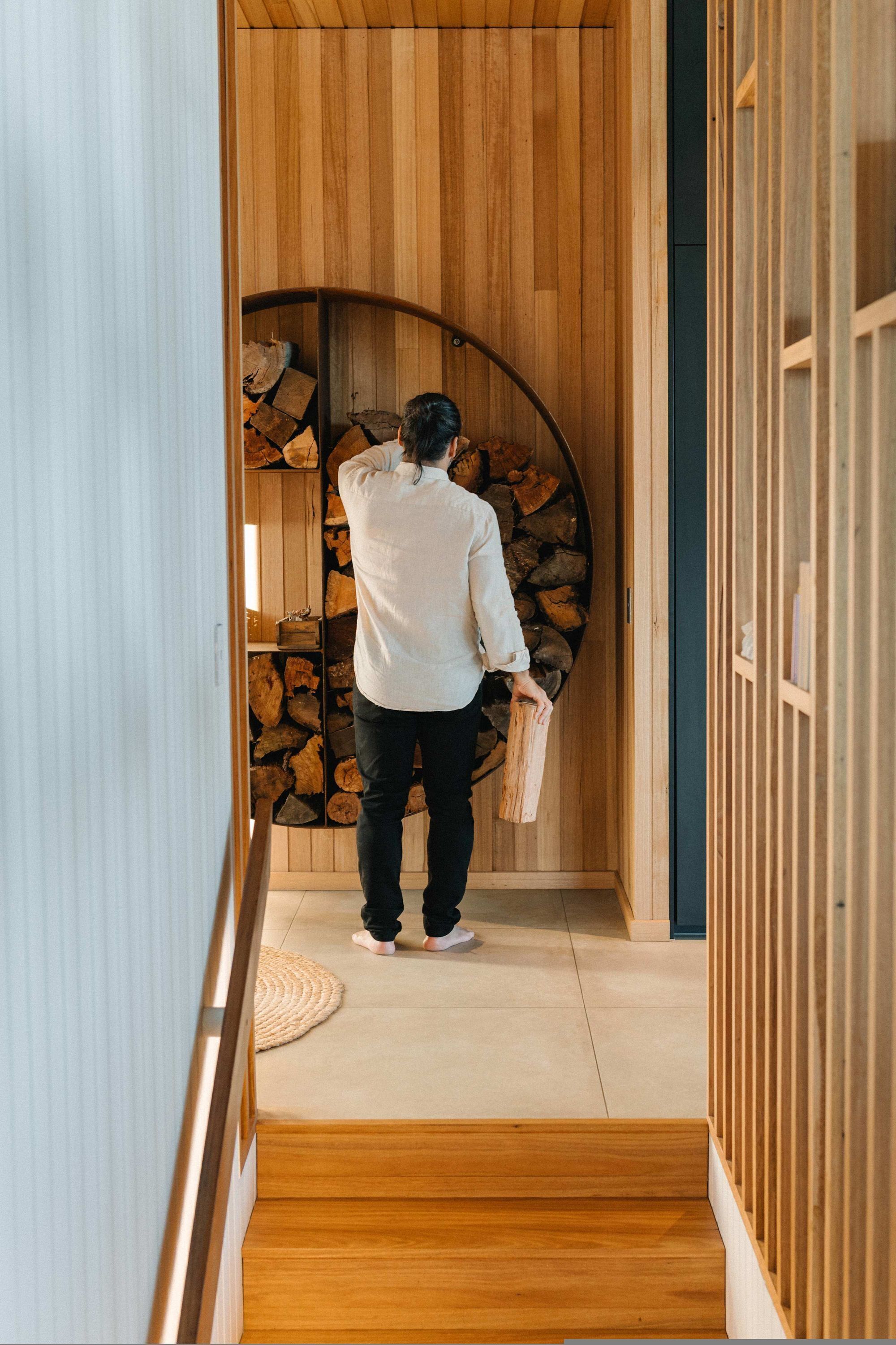 A person carrying a log through a wooden hallway with a built-in log storage area.