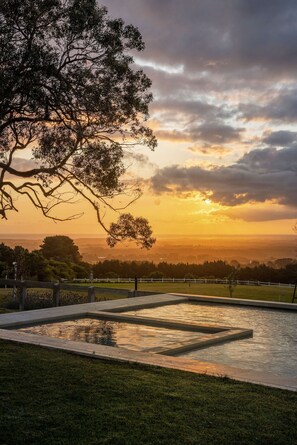 A rectangular pool with a geometric pattern, surrounded by a white fence, set against a sunset with clouds in the sky. - Villa Floretti Heated Spa With Stunning Views (Melbourne)
