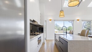 A modern kitchen with white cabinets, a large island, and pendant lighting. - Saltwood Coastal Hamptons Luxe With Pool (Melbourne)